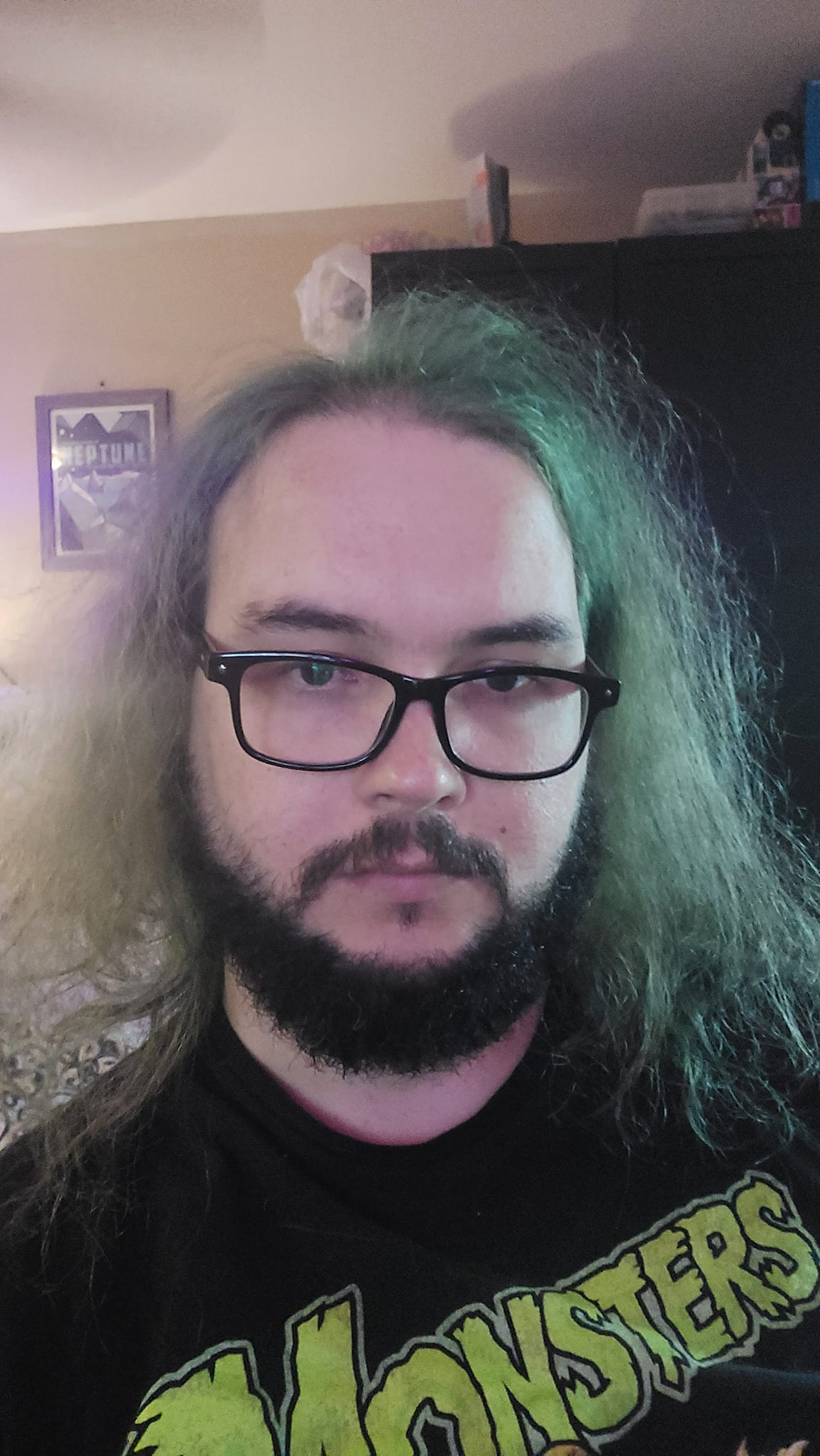 A man with green hair and a beard sits in a computer chair with a tired, dazed look